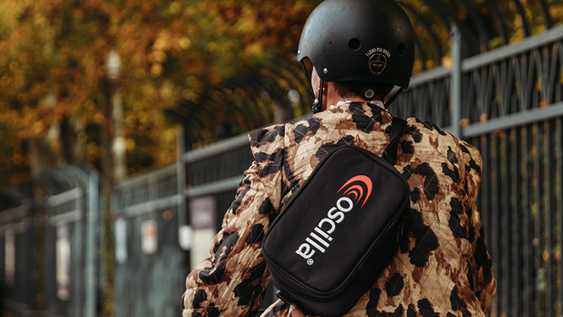 Person carrying Oscilla portable diagnostic audiometer in a shoulder case, highlighting mobile hearing screening capability.