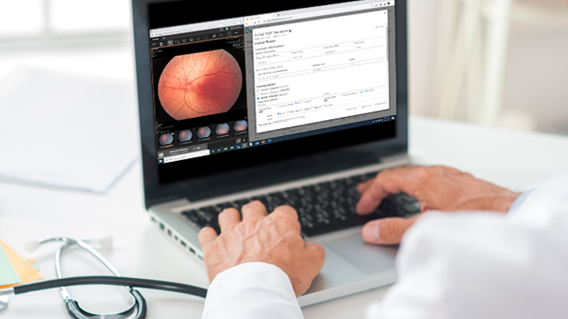 Physician using a laptop to review retinal imaging and screening data via DataLink and RetCam Envision, enabling cloud-based remote diagnostics and reporting.